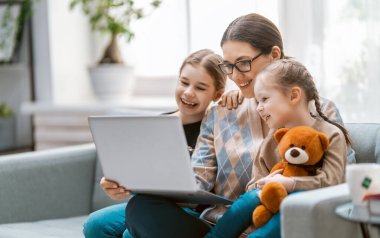 Sevgi dolu bir aile. Laptop kullanan genç anne ve kız çocukları. Komik anne ve güzel çocuklar evde kalarak eğleniyorlar..