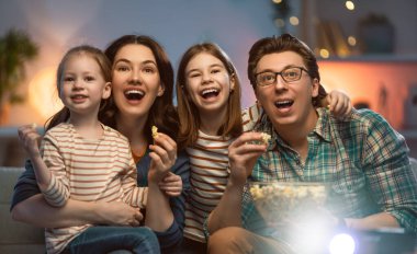 Mutlu aile projektörü, TV, akşam evde patlamış mısırlı filmler. Anne, baba ve kızları birlikte vakit geçiriyorlar..