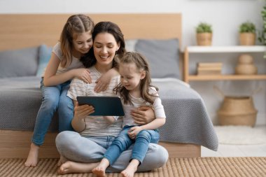 Sevgi dolu bir aile. Genç anne ve kızları arkadaşlarıyla uzaktan konuşmak için tablet bilgisayar kullanıyorlar. Komik anne ve güzel çocuklar evde kalarak eğleniyorlar..