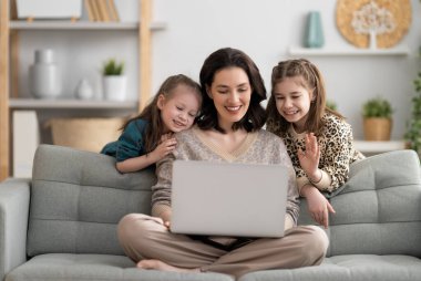 Sevgi dolu bir aile. Laptop kullanan genç anne ve kız çocukları. Komik anne ve güzel çocuklar evde kalarak eğleniyorlar..