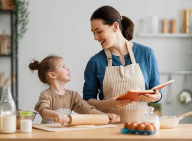 Mutlu aile birlikte fırın hazırlıyor. Anne ve kız çocuk kurabiye pişiriyor ve mutfakta eğleniyorlar. Ev yapımı yemek ve küçük bir yardımcı..   