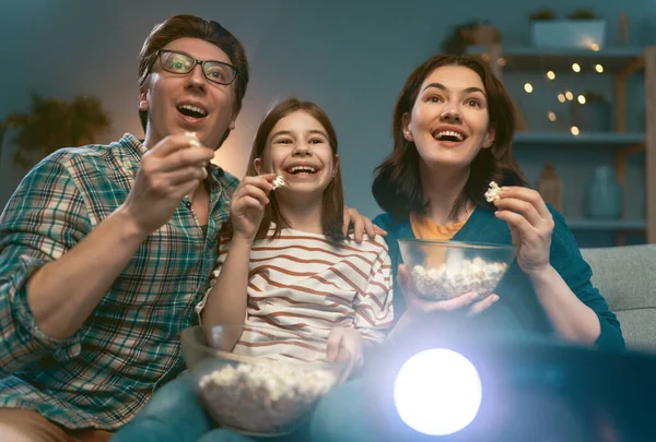 Mutlu aile projektörü, TV, akşam evde patlamış mısırlı filmler. Anne, baba ve kızı birlikte vakit geçiriyorlar..