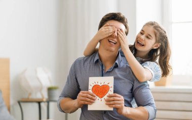 Babalar günün kutlu olsun! Çocukların kızları babalarını tebrik ediyor ve ona kartpostal veriyorlar. Baba ve kızlar gülümsüyor ve sarılıyorlar. Aile tatili ve birliktelik.