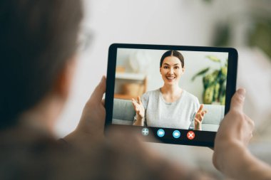 Genç adam bir kadınla uzaktan konuşmak için tablet kullanıyor. İnsanlar evde kalarak eğleniyor..