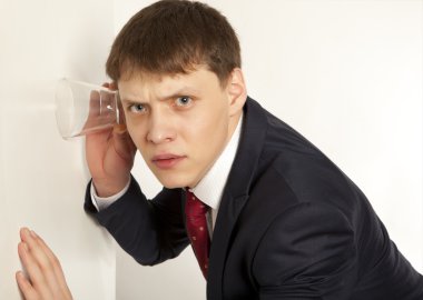 Businessman spying by listening through wall with glass clipart