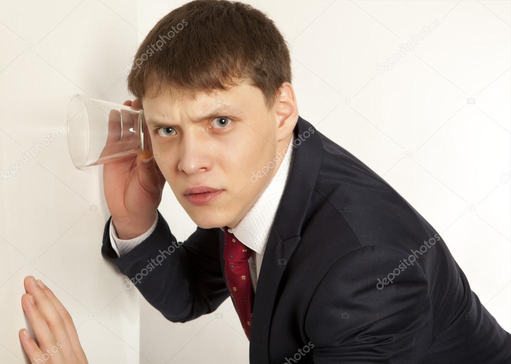 Businessman spying by listening through wall with glass