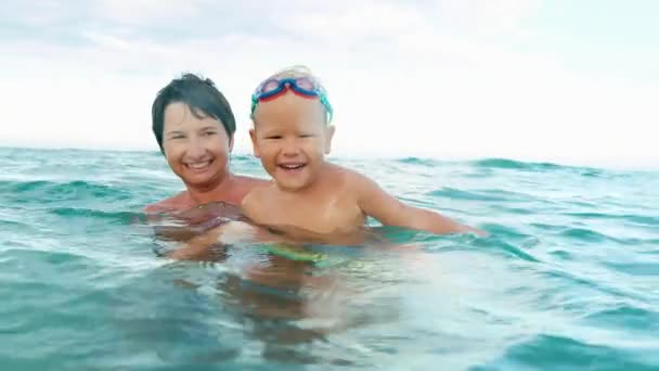 Gelukkige zoon en moeder lacht, camera kijken, maken van plons in de zee slow motion — Stockvideo