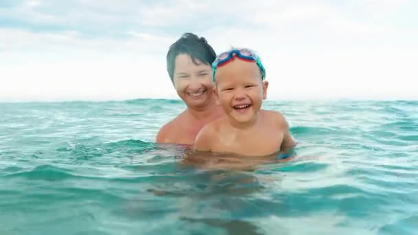 Filho feliz e mãe sorrindo, olhando para a câmera, fazendo respingo no mar câmera lenta — Vídeo de Stock
