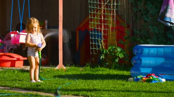 Маленька дівчинка поливає газон — стокове відео