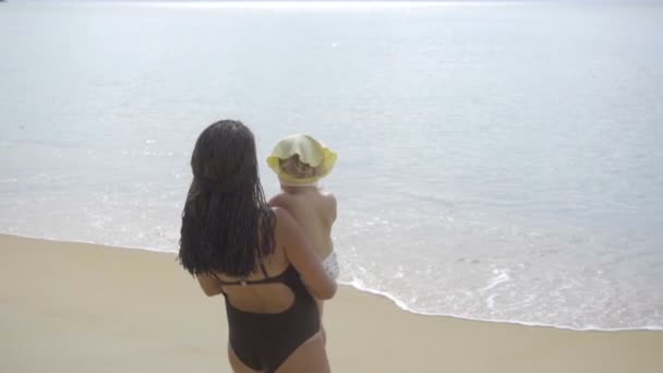 Maman avec une fille de deux ans marchant le long de la plage de sable — Video