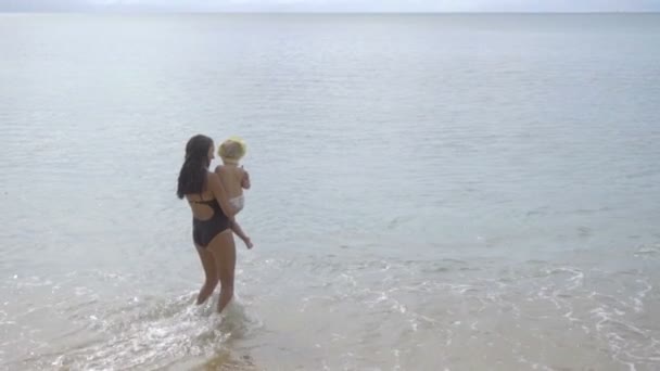 Maman avec une fille de deux ans marchant le long de la plage de sable — Video