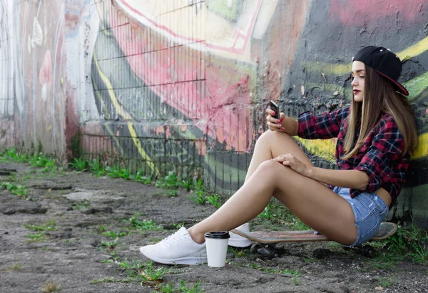 Teini tyttö etsii puhelimeen istuessaan rullalaudoilla — kuvapankkivalokuva
