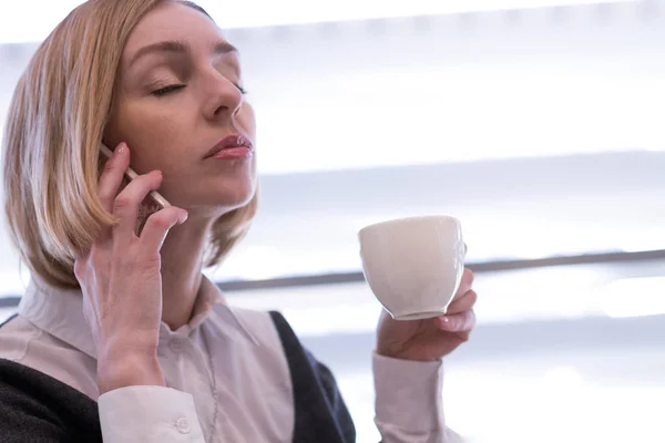 Уставшая женщина пьет кофе и звонит — стоковое фото