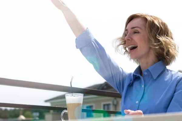 Красивая современная женщина пьет кофе в кафе и приветствует кого-то — стоковое фото