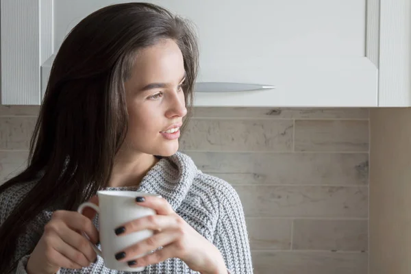 Nuori moderni nainen brunette juo teetä keittiössä — kuvapankkivalokuva