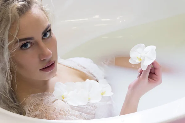 Aantrekkelijke vrouw in de badkamer met bloemen en melk — Stockfoto
