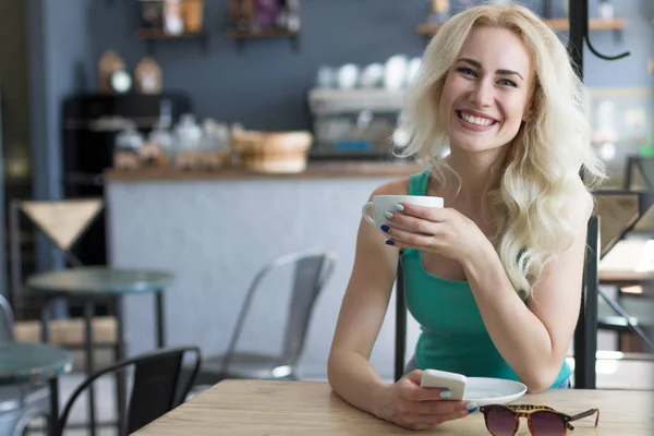 Счастливая женщина пьет кофе и пользуется телефоном — стоковое фото