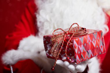 Noel Baba kırmızı arka plan kırmızı bir hediye sunuyor