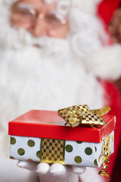 Weihnachtsmann bietet ein rotes Geschenk vor rotem Hintergrund — Stockfoto