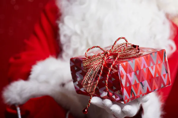 Santa claus erbjuder en röd gåva mot röd bakgrund — Stockfoto