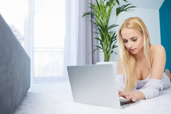 Sorrindo mulher deitada no tapete usando seu laptop — Fotografia de Stock