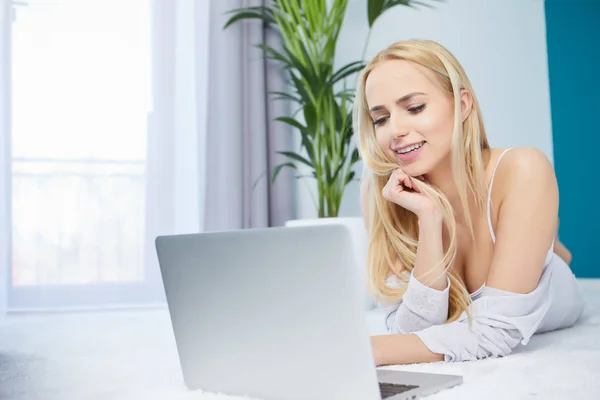 Sorrindo mulher deitada no tapete usando seu laptop — Fotografia de Stock