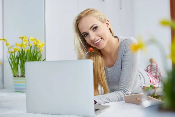 Sorrindo mulher deitada no tapete usando seu laptop — Fotografia de Stock