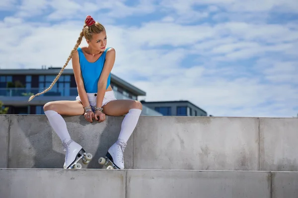 Linda menina loira em um maiô em patins sentados em um — Fotografia de Stock