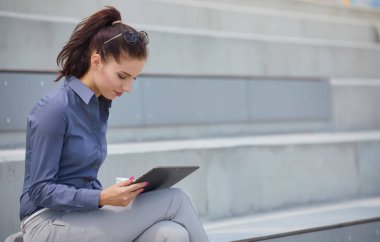 İşkadını bir tablet ile beton duvara oturur. 