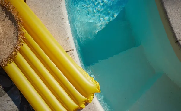 Materac i kapelusz leżą na skraju basenu. — Zdjęcie stockowe