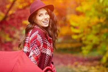 Sonbahar parkında şemsiyeli bir kadın yürüyor.