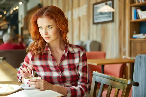Kızıl saçlı kadın kahve dükkanında kitap okumak gülümseyen