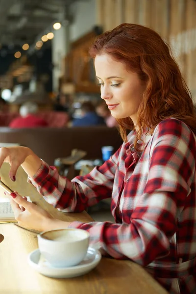 Kızıl saçlı kadın kahve dükkanında kitap okumak gülümseyen