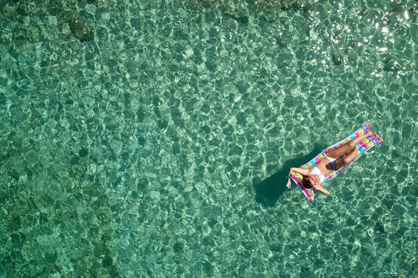 明るいビキニの若い女性の平面図は 透明な青い海で泳いでいます 横になっていると 水に浮いてにスリムな女性の空撮 — ストック写真