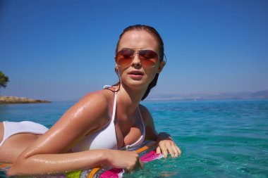 kız mavi güneşli gökyüzü karşı sahilde. Pembe bir şişme yatak, güneş gözlüğü, holding ıslak deri tabaklama. Dinlenme, Güney, resort, plaj. Güneşli gün.