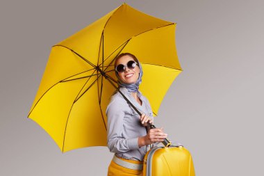 Glamour woman with yellow umbrella and suitcase. Travel concept