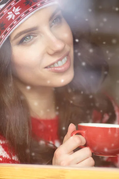 Frau trinkt Kaffee und schaut im Winter aus dem Fenster — Stockfoto