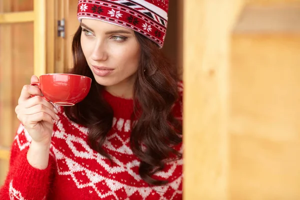 Mujer usando un suéter y sombrero sosteniendo taza de bebida caliente —  Fotos de Stock