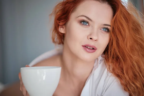 Atractiva mujer pelirroja con una taza de café en la cama — Foto de Stock