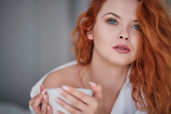 Belle femme rousse avec une tasse de café sur le lit — Photo