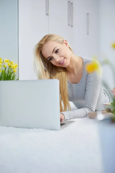 Young woman lying with laptop on the carpet — Stock Photo, Image