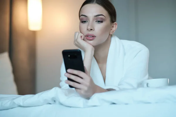 Das Mädchen im Bett. Sie schaut auf das Smartphone. Einfluss der Sozialisten — Stockfoto