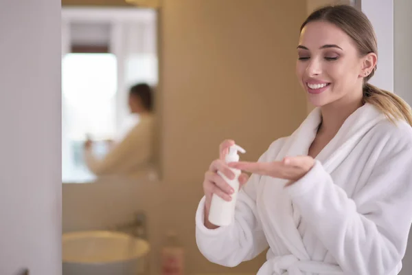 A woman in a bathrobe applies body cream — 스톡 사진