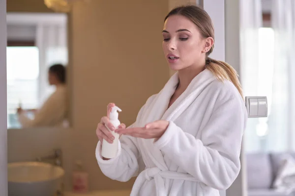 A woman in a bathrobe applies body cream — 스톡 사진