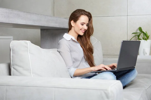 Mulher usando um laptop enquanto relaxa no sofá — Fotografia de Stock