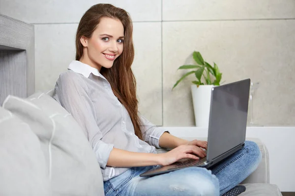 Vrouw met behulp van een laptop terwijl ontspannen op de bank — Stockfoto