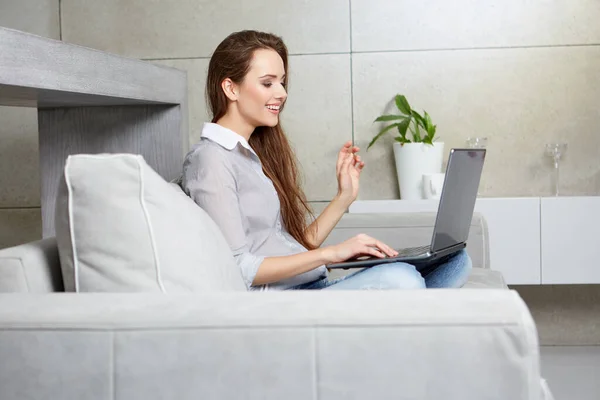 Mulher usando um laptop enquanto relaxa no sofá — Fotografia de Stock