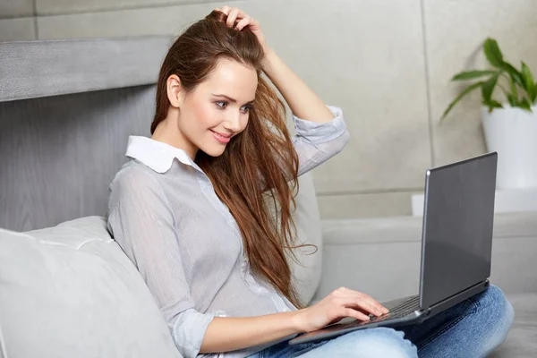 Mulher usando um laptop enquanto relaxa no sofá — Fotografia de Stock