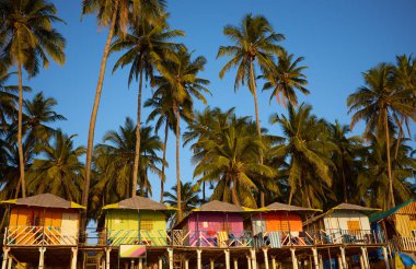 Colorful huts on the sandy beach with palm trees background in G clipart