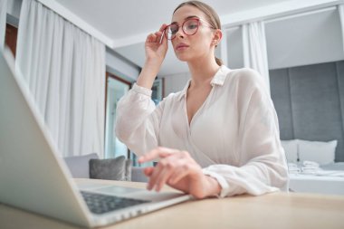 Gözlüklü kadın kanepeye oturmuş, dışarıya bakıyor, işine konsantre olamıyor, dinlenmeye ihtiyacı var, canı sıkılıyor, ek motivasyona ihtiyacı var, uzaktan evde çalışıyor..